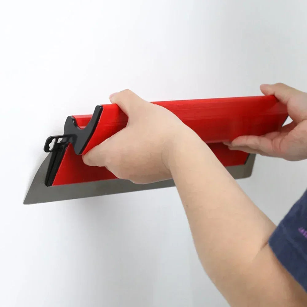 A hand is holding a red and silver skimming blade against a white wall for finishing work.