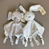 A white elephant plush toy with ears, a teether, and a comfort blanket, lying on a gray surface.