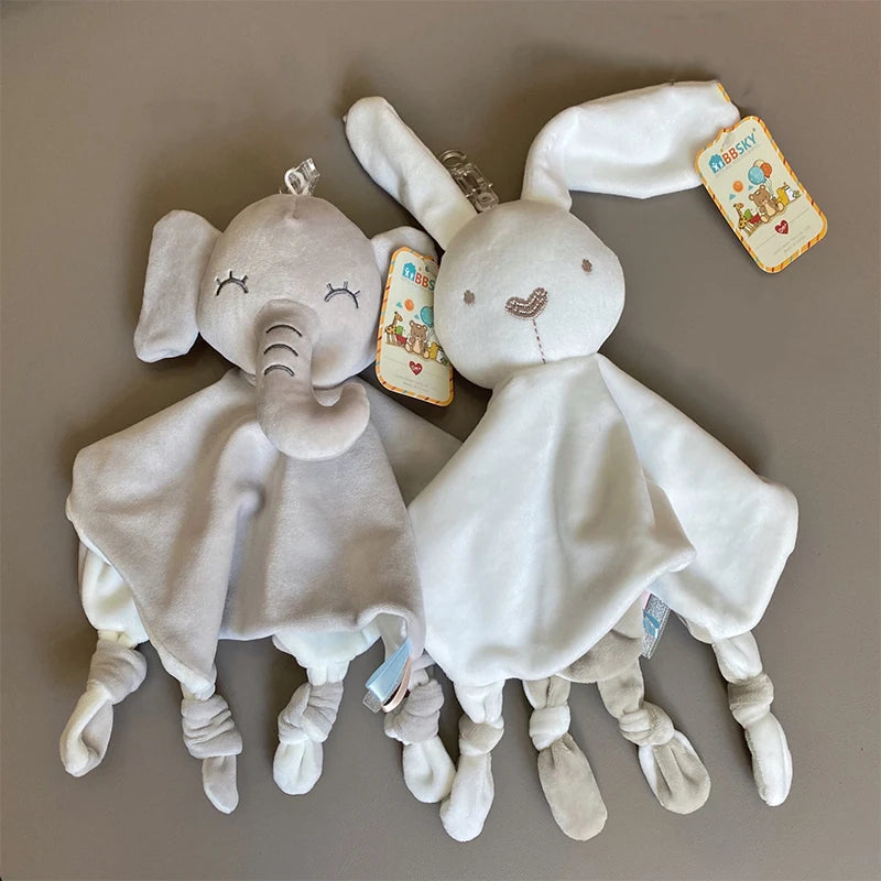A white elephant plush toy with ears, a teether, and a comfort blanket, lying on a gray surface.