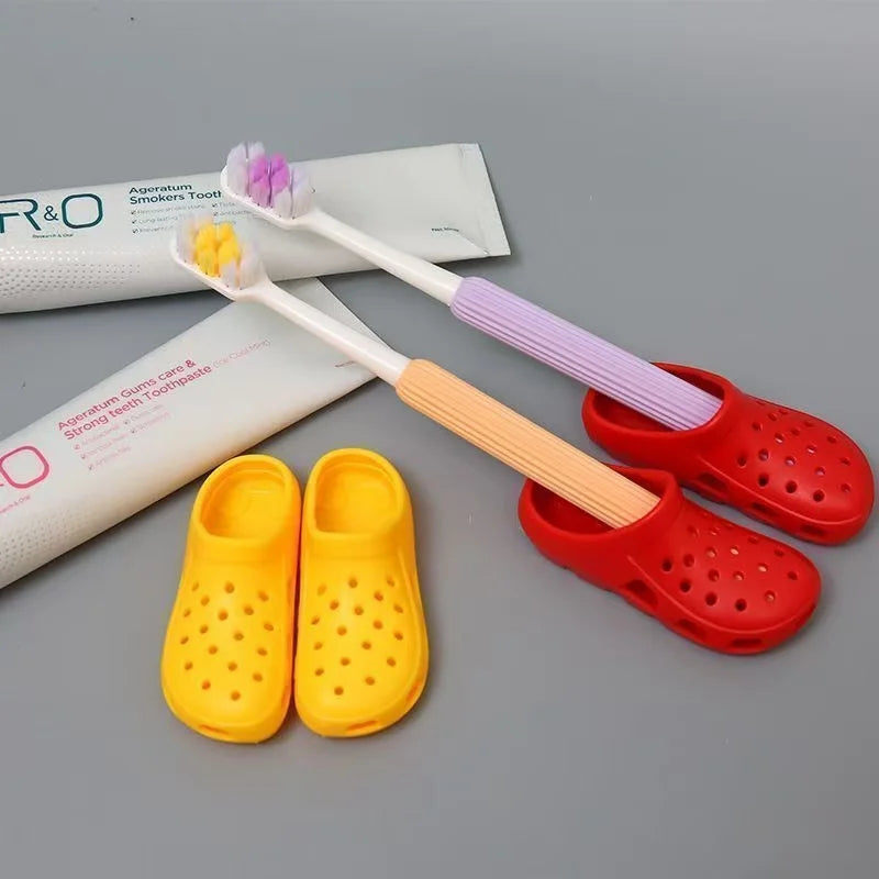A set of silicone toothbrush holders and a wooden toothbrush with purple bristles are displayed next to a white packaging box