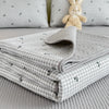 A stack of light gray floral quilted linens and a small cream stuffed rabbit toy on a bed.