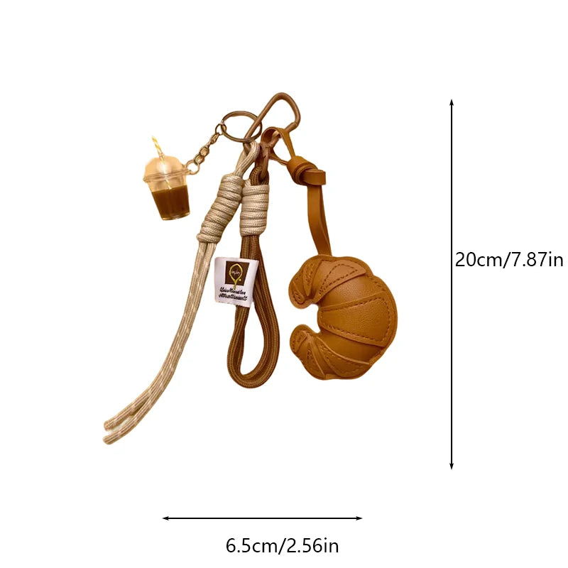 A braided leather croissant keychain featuring a bag pendant and a small glass charm.