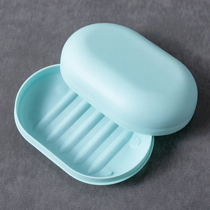 A light blue portable soap dish with a lid is shown in an open angle on a gray surface.