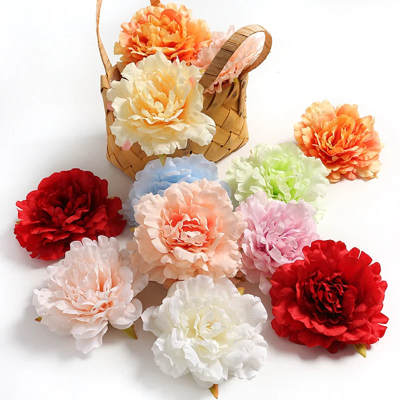 A collection of silk peony flower heads in shades of orange, pink, peach, and white are displayed in a woven basket.