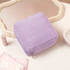 A lavender ribbed storage pouch with a zipper is displayed on a white surface next to a mirror frame and pink sanitary napkin