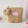 A beige cosmetic bag with a leopard print texture and gold hardware, shown against a white background.