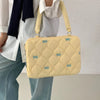 A light yellow quilted laptop shoulder bag with blue bows is carried by a person wearing a white shirt and jeans.