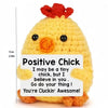A yellow crochet chick doll with a red tuft on its head and a positive message card.