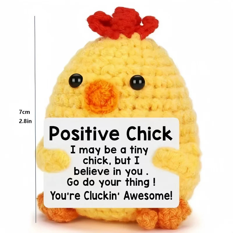 A yellow crochet chick doll with a red tuft on its head and a positive message card.