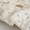 A close-up of a cream floral muslin baby blanket with delicate pink and green floral patterns.