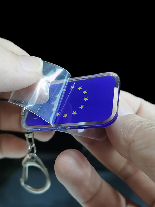 Eine Hand hält einen eleganten Acryl-Anhänger mit dem Design der blauen und gelben EU-Flagge.