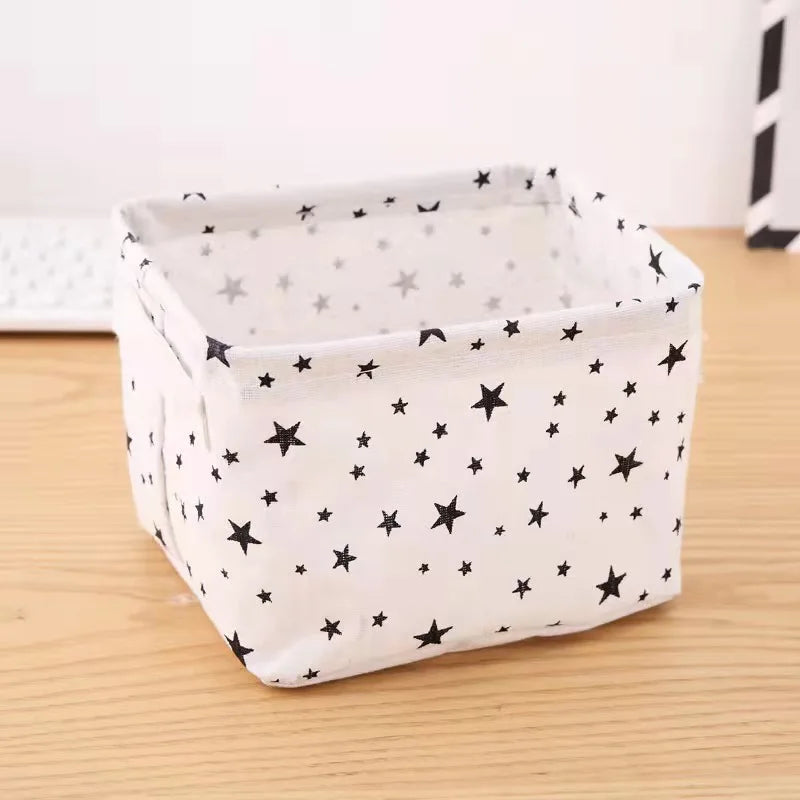 A white storage basket with a lid and handles decorated with black stars on a wooden surface.