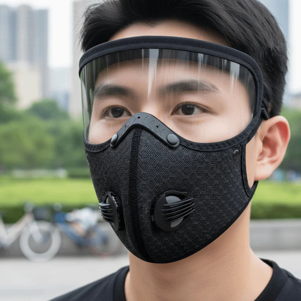 A close-up of a person wearing a black reusable cycling face mask with a clear shield over their face.