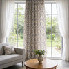 A window dressed with a beige and blue floral cotton-linen curtain featuring tassels, letting in natural light.