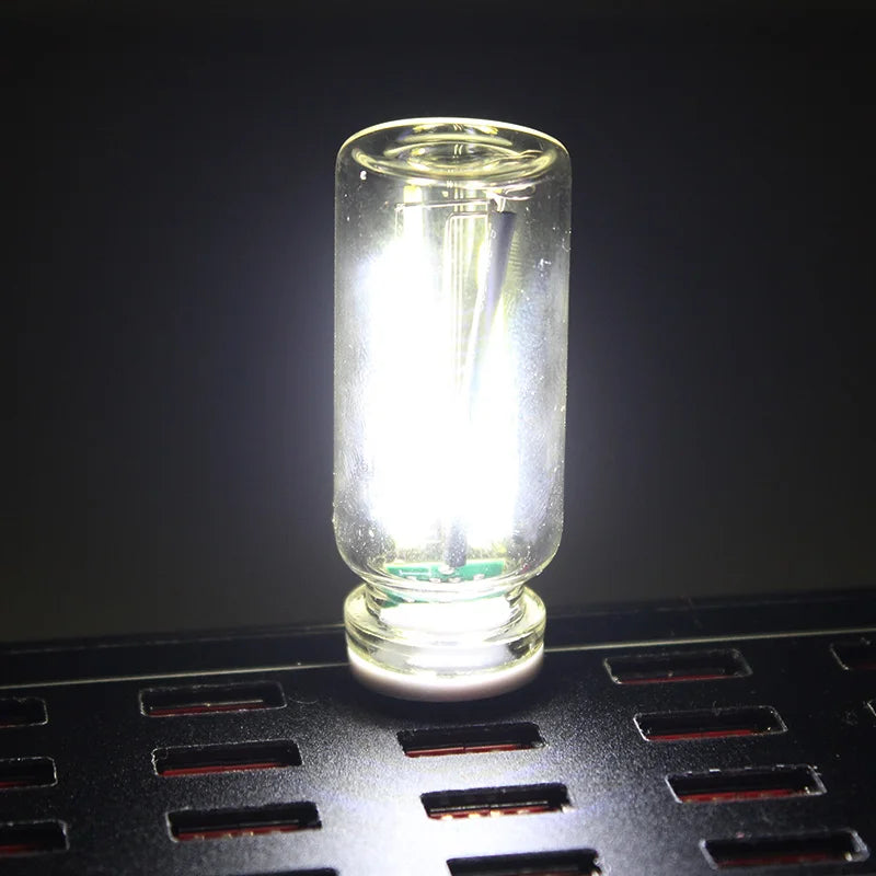 A clear glass accent light bulb resting on a black grid surface.