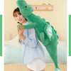A woman is holding a large, green dragon plush toy against her chest in a light blue shirt.