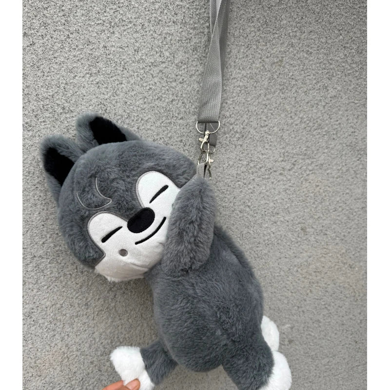 A gray and white plush toy resembling a stylized animal face is hanging against a gray textured background.