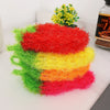 A stack of brightly colored strawberry scrubber sponges in red, yellow, and green are displayed next to a bottle.