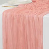 A flowing, dusty rose cotton gauze table runner with gathered texture and draped folds.