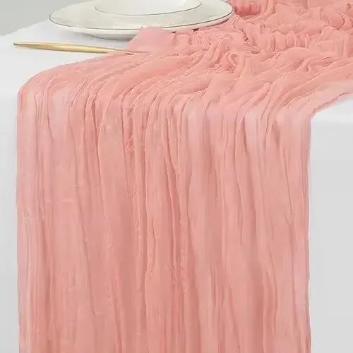 A flowing, dusty rose cotton gauze table runner with gathered texture and draped folds.