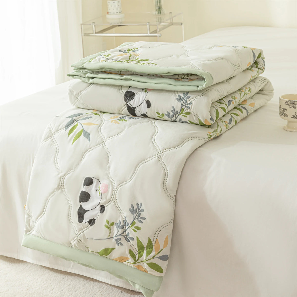 A white quilted summer quilt featuring a floral pattern with black and white panda designs on a bed.