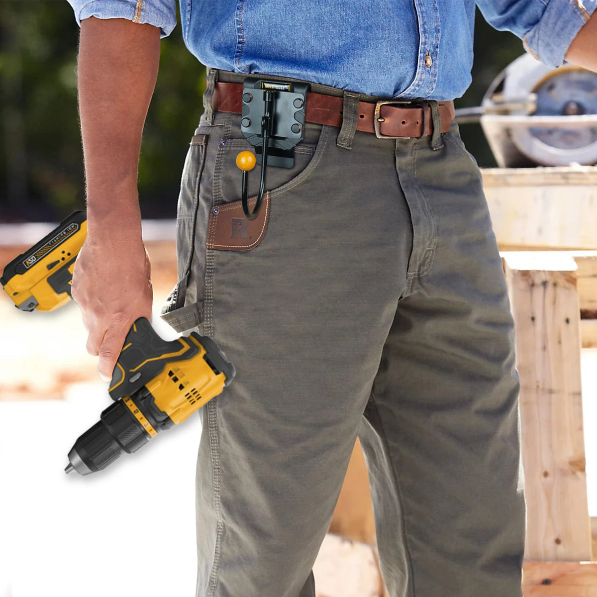 A person wearing denim shirt and jeans is holding a yellow rotating tool belt hook attached to a leather belt.
