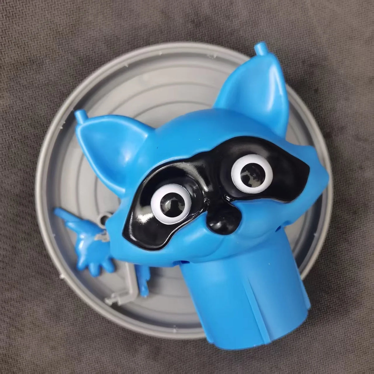 A blue plastic animal toilet paper holder with large black eyes is shown on a silver circular plate.
