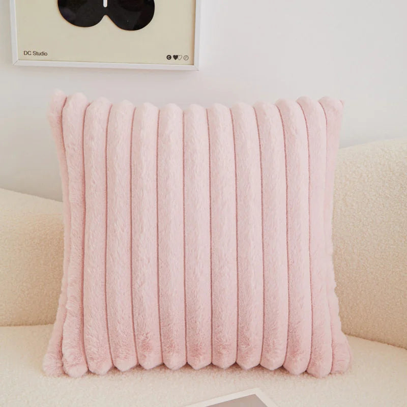 A pink, vertically ribbed plush decorative pillow cover resting on a light-colored sofa.