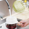 A hand is holding a white fruit washing basket with a strainer over a sink, draining fruit.