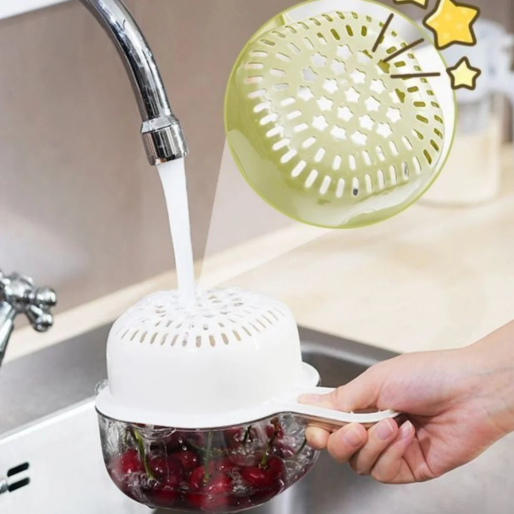 A hand is holding a white fruit washing basket with a strainer over a sink, draining fruit.