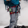 A person wearing gray pants and a teal shirt is equipped with gear, including a braided paracord work glove clip and carabine
