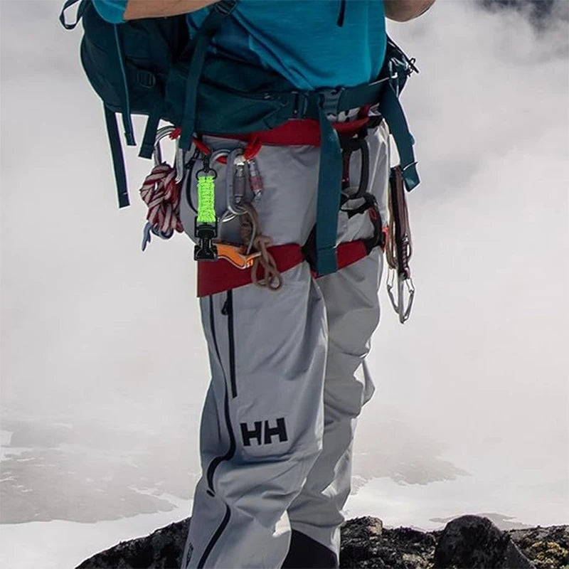 A person wearing gray pants and a teal shirt is equipped with gear, including a braided paracord work glove clip and carabine