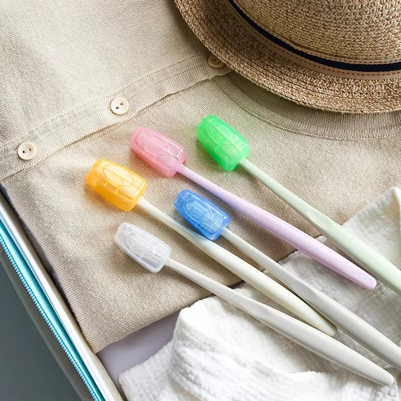 A set of colorful protective toothbrush heads with travel clips displayed on a beige fabric next to a straw hat.