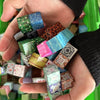 A hand holds a collection of colorful magnetic building blocks in various shades of green, blue, pink, and brown.