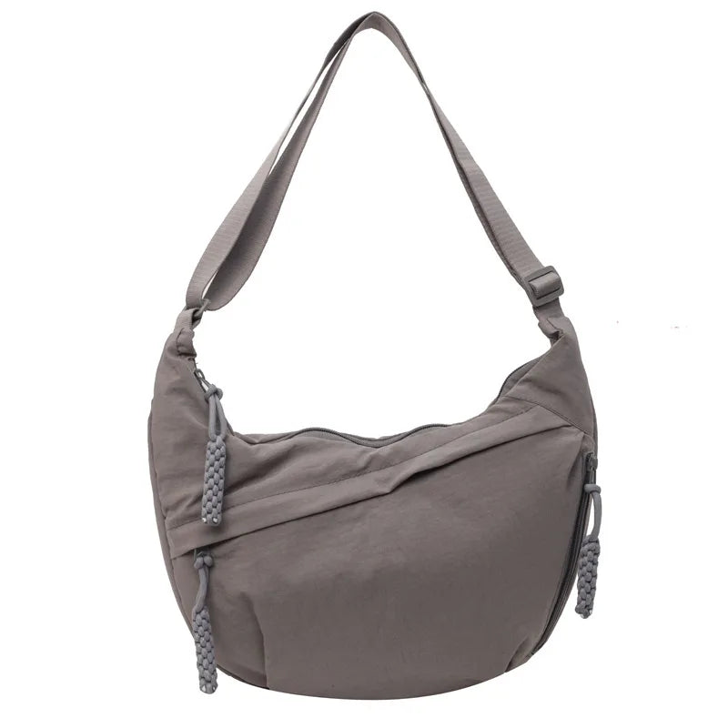 A light gray nylon crossbody bag with an adjustable strap shown from the front.