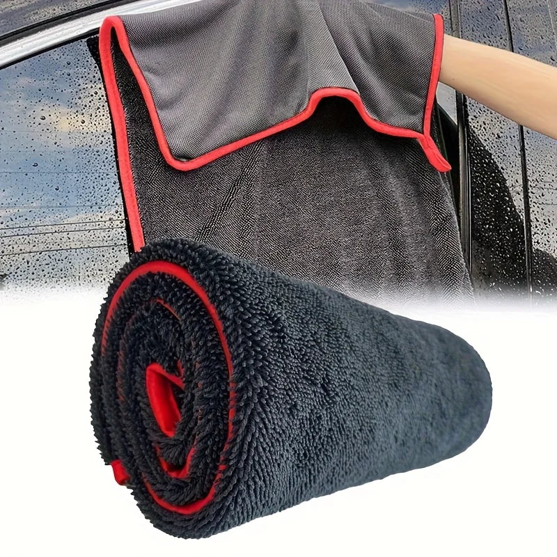 A rolled black microfiber drying towel with red trim is shown next to a car door.