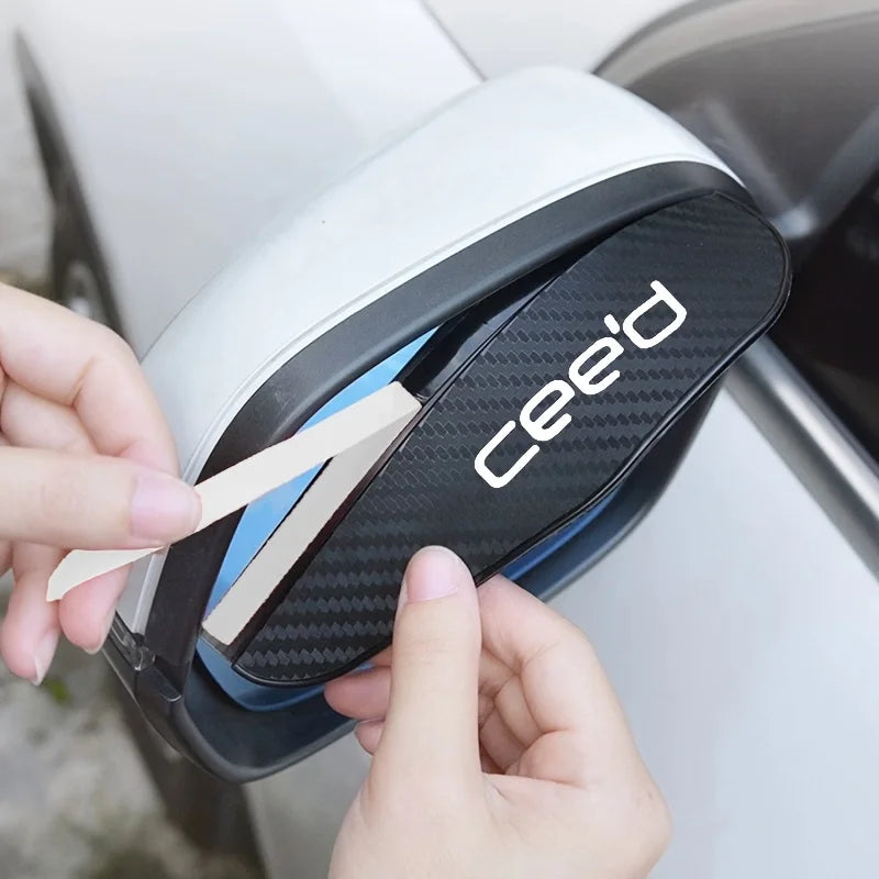 A hand is removing a carbon fiber rain guard from a white car's rearview mirror.