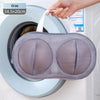 A hand is placing a gray mesh laundry bag into the drum of a washing machine.