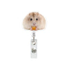 A fluffy light brown hamster is holding a piece of orange food while interacting with a retractable badge reel.