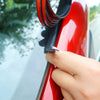 A hand is applying a black rubber seal strip to the edge of a red car window frame.
