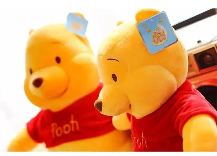 A yellow Winnie the Pooh plush toy wearing a red shirt and a blue badge.