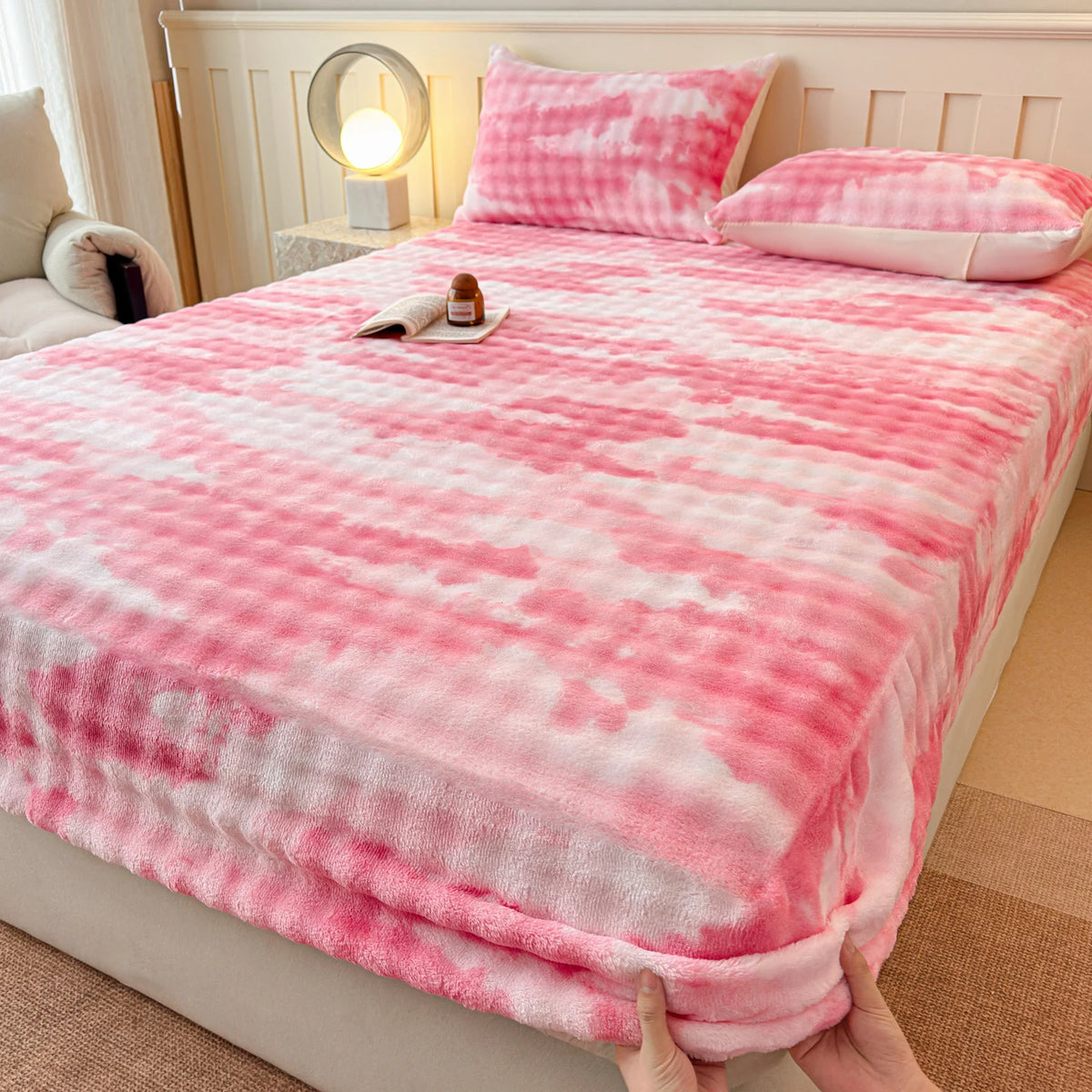 Pink and white faux fur fitted sheet spread on a bed with pillows and a bedside lamp.