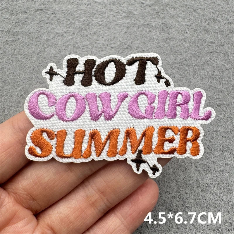 Embroidered patch featuring the text HOT COW GIRL SUMMER in brown, purple, and orange thread on a light fabric background.