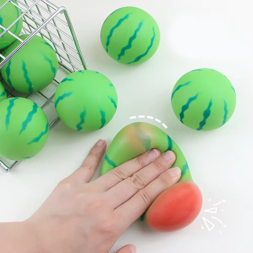 Eine Hand drückt ein wassermelonenförmiges Stressabbau-Spielzeug, umgeben von ähnlichen Spielzeugen und einem Drahtkorb.