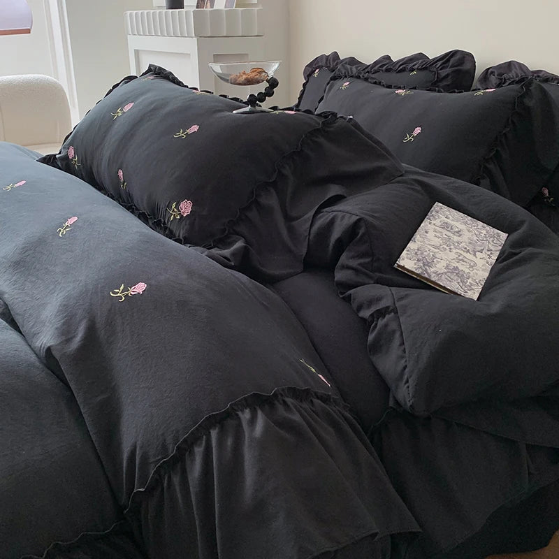 A black duvet cover set with rose embroidery and lace details is displayed on a bed.