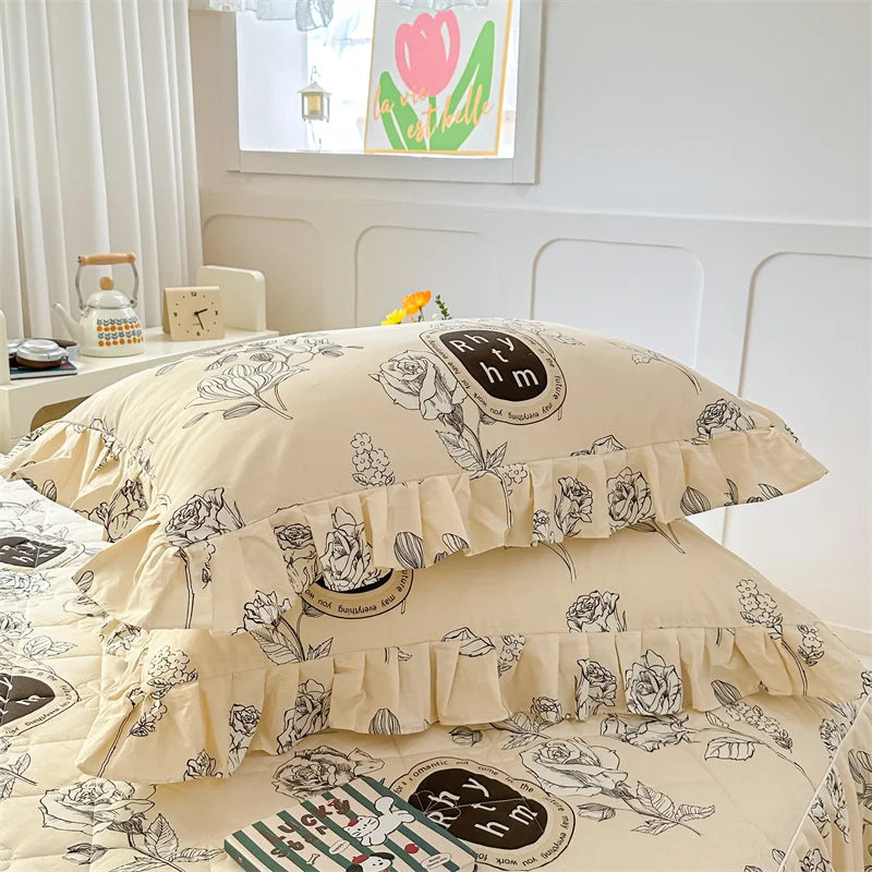 A set of two floral cotton pillowcases with ruffled edges and a pattern featuring roses and greenery.