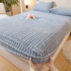 A hand is pulling down a light blue, ribbed faux fur fitted sheet on a bed.