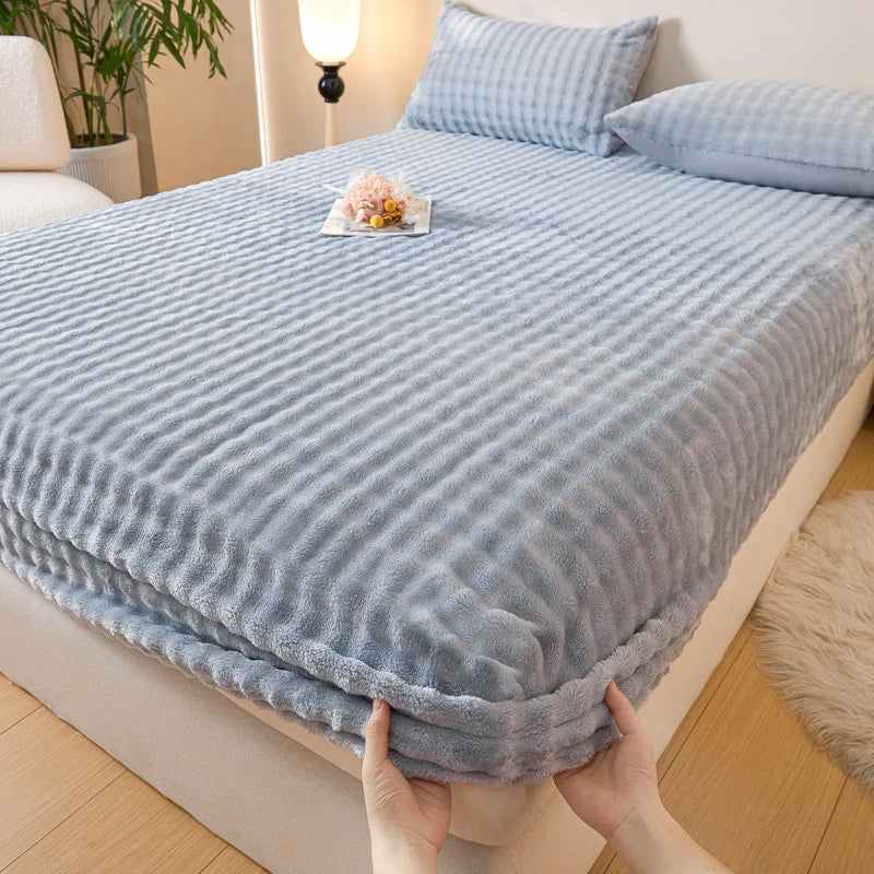 A hand is pulling down a light blue, ribbed faux fur fitted sheet on a bed.