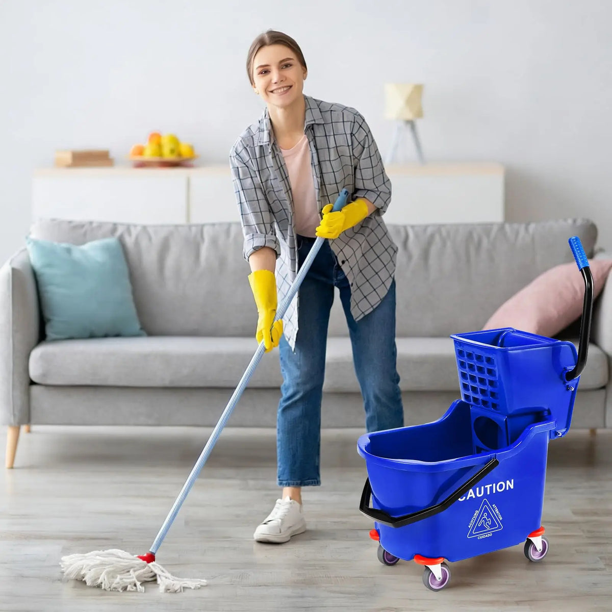A woman is using a blue rolling mop bucket and pole to clean a floor.