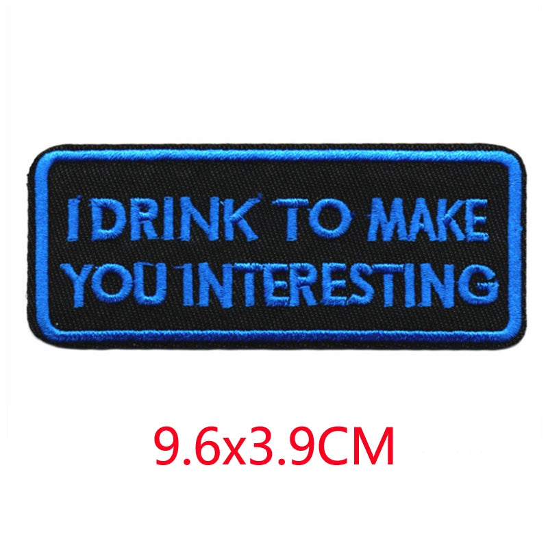 A rectangular dark blue embroidered iron-on letter patch with white text that reads I DRINK TO MAKE YOU INTERESTING